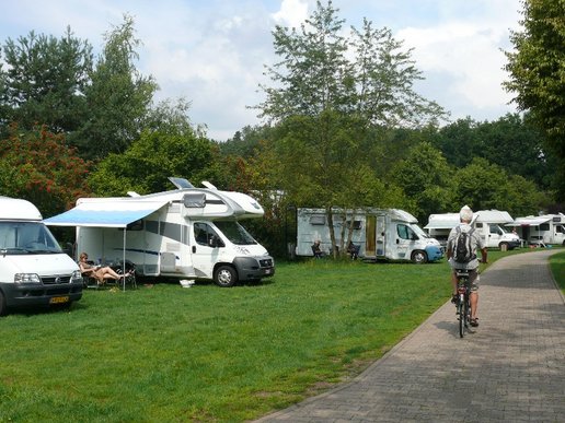 Einige geparkte Wohnmobilde auf einer Wiese, ein Fahrradfahrer fährt auf einem angrenzenden Weg entlang